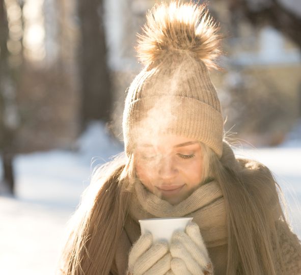 Young woman drink hot tea walking in snowy park on sunny cold winter morning enjoy frosty weather