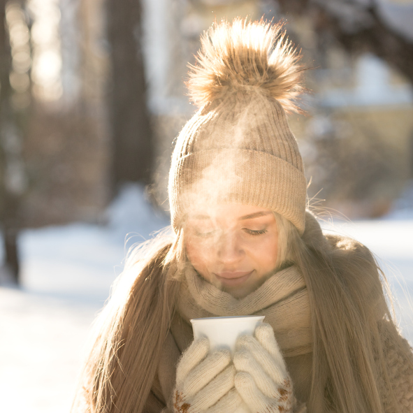 Young woman drink hot tea walking in snowy park on sunny cold winter morning enjoy frosty weather