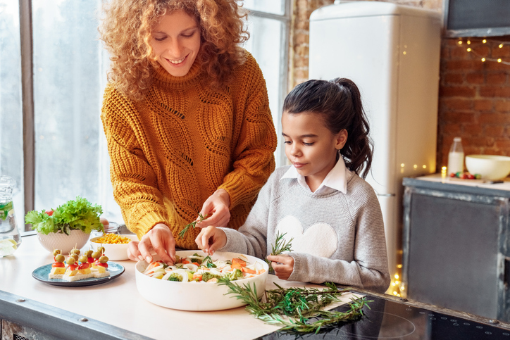 Happy curly woman and a girl niece making healthy vegan food for family feasting