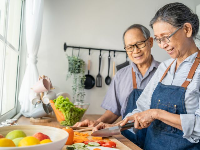 Asian loving senior elderly couple wear apron and cooking in kitchen. Attractive strong old man and woman grandparent wear eyeglass enjoy retirement life activity at home. Family relationship concept.
