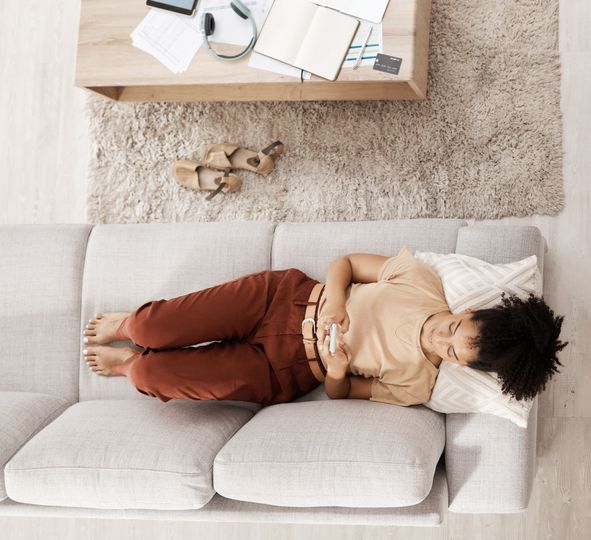 Black woman with smartphone, relax on couch and social media scroll overhead, taking break from work or study with communication and tech. Break, rest after bills or online shopping and mobile app