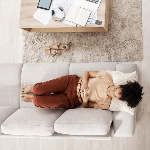 Black woman with smartphone, relax on couch and social media scroll overhead, taking break from work or study with communication and tech. Break, rest after bills or online shopping and mobile app