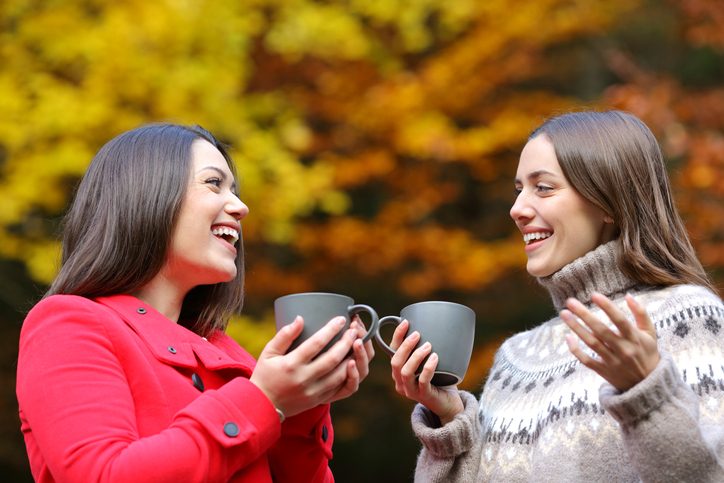 Happy friends talking with coffee mugs in a park