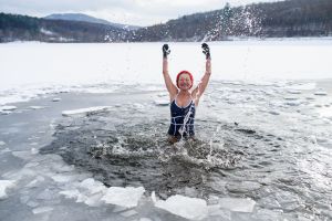 Active senior woman in swimsuit splashing water outdoors in winter, cold therapy concept.